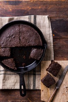 a chocolate cake in a cast iron skillet on a wooden table next to a knife