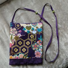 a small purse is sitting on a bed with a purple strap around the shoulder and has flowers all over it