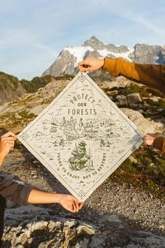 two people holding up a sign on top of a mountain