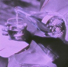 a person pouring something into a glass in front of a purple and black background with the image of a man's hand holding an object