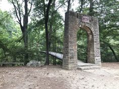 a stone arch in the middle of a forest with stairs leading up to it and trees around