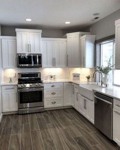 a large kitchen with white cabinets and stainless steel appliances, including an oven, dishwasher, microwave, stove and sink