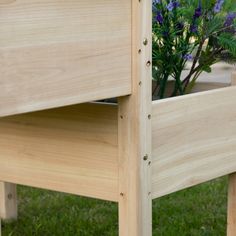 a wooden planter with purple flowers in it on the grass next to a bench