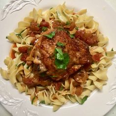 a white plate topped with pasta and meat covered in sauce, garnished with parsley