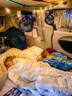 two children are sleeping in the back of a car with their blankets pulled up and lights on