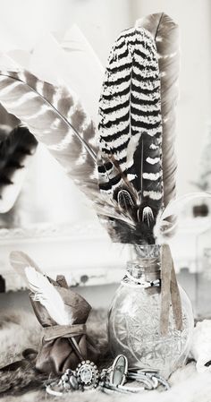 some feathers are in a glass vase on a table next to other items and decorations