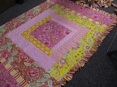 a pink and yellow quilt on the floor next to a vase with flowers in it