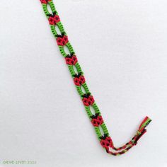 a green and red bracelet on a white surface with a black bead chain attached to it