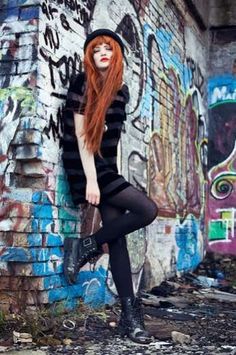 a woman with long red hair standing in front of a graffiti covered wall