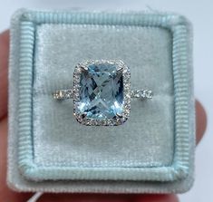 someone is holding an engagement ring with a blue topazte surrounded by white diamonds