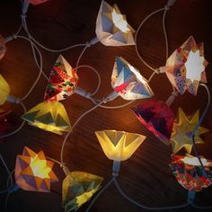 many colorful paper flowers are hanging on a string with some lights attached to the strings