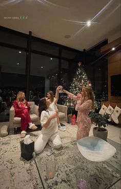 three women are sitting on the floor in front of a christmas tree