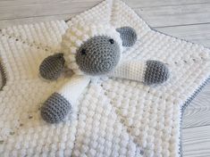 a crocheted sheep laying on top of a white blanket next to a wooden floor