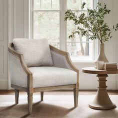 a white chair sitting next to a vase with a plant in it on top of a table