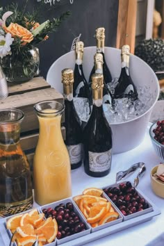 bottles of champagne, orange slices and cranberries are on a table with flowers