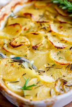 a close up of a dish of food with potatoes and herbs in it on a wooden table