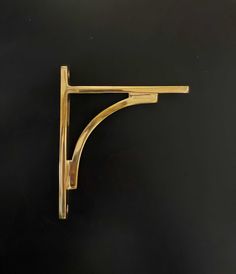 a brass shelf bracket on a black wall with the top half turned to look like it has been made out of wood