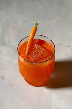 an orange drink in a glass with a carrot on the rim and garnish