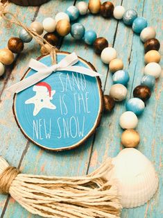 a wooden sign that says sand is the new snow on it next to some seashells