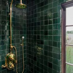 a green tiled shower with gold faucet and hand held shower head in the corner