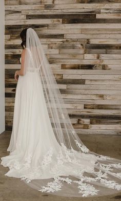 a woman in a wedding dress standing next to a wooden wall wearing a long veil