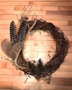 a close up of a wreath on a wooden floor with feathers and pineconis