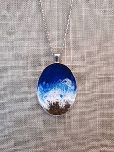 a blue and white necklace with mountains in the background on a silver plated chain