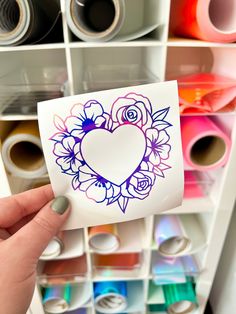 someone is holding up a sticker with a heart and flowers on it in front of some crafting supplies