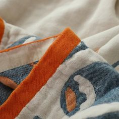 an orange, white and blue blanket laying on top of a bed next to a pillow