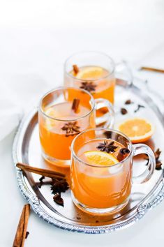 two mugs filled with orange juice and cinnamon on a silver tray next to anisette