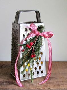 an old metal grater with holly and berries tied around it, sitting on a wooden table