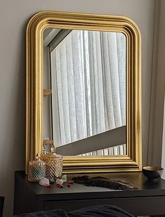 a gold framed mirror sitting on top of a dresser