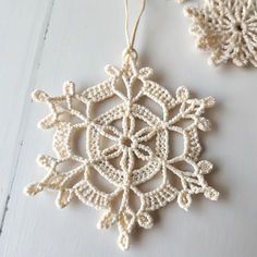 a crocheted snowflake ornament hanging from a string on a white wall