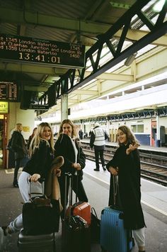 three women are standing with their luggage at the train station