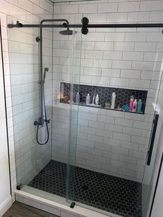 a walk in shower sitting next to a white tiled wall with shelves on each side