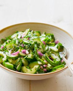 a bowl filled with cucumbers and onions on top of a wooden table next to a spoon