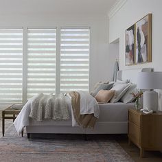 a white bed sitting in a bedroom next to a window with blinds on it's sides