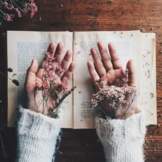 someone is holding flowers in their hands over an open book on a wooden table with dried flowers