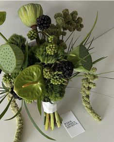 a vase filled with lots of green flowers on top of a white table next to plants