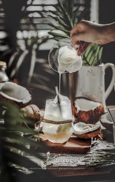 someone pouring ice cream into a glass on top of a cutting board next to coconuts