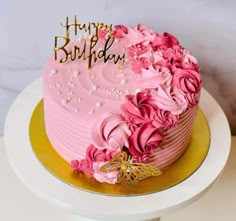 a pink birthday cake with gold lettering and flowers on top is sitting on a plate