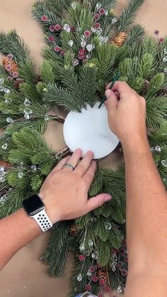 someone is decorating a christmas wreath with pine cones and other greenery around it