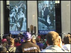 people are standing in front of two large posters on the side of a building,