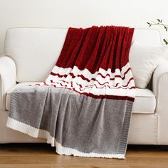 a white couch with a red and grey blanket on it's back next to a plant