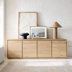 a white brick wall and wooden furniture in a living room with an art work on the sideboard