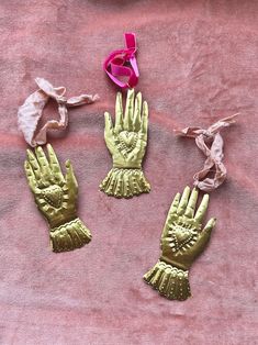 three pairs of gold colored gloves on a pink cloth