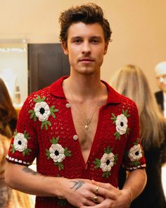 a man in a red shirt with white flowers on his chest and tattoos on his arm