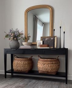 a console table with two baskets on it and a mirror in the corner next to it