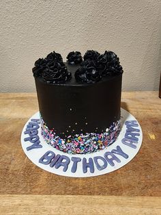 a birthday cake with black frosting and sprinkles on a wooden table