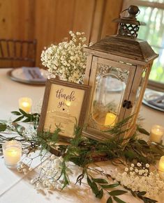 the table is set with candles, flowers and an old - fashioned lantern on it